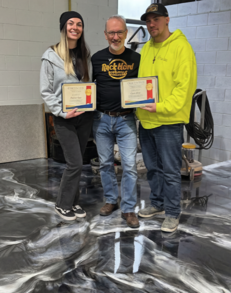 Ryan and Amanda receiving their XPS epoxy certification, standing on a stunning metallic epoxy floor